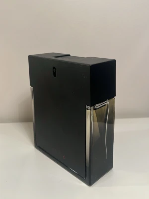 Svart rektangulär parfymflaska - Stilren mansparfym i svart och transparent glas med rektangulär form. Flaskan har en modern design med mattsvart front och sidor i klart glas som visar vätskan inuti. Perfekt för dig som gillar minimalistisk och elegant stil. Endast använd få gånger se bild