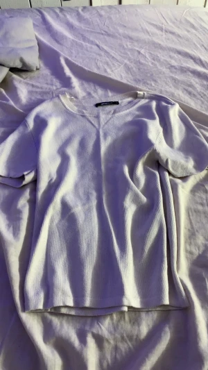 Vit ribbad topp med kort ärm - En enkel och stilren vit topp med ribbad struktur och korta ärmar. Toppen har rund halsringning och är gjord i ett mjukt material som känns skönt mot huden. Perfekt att matcha med jeans eller kjol för en clean look.