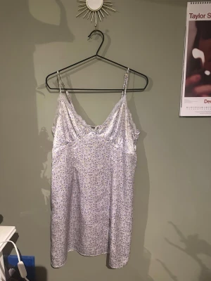 Blommigt nattlinne med spetsdetaljer - Söt kort klänning med tunna axelband och blommigt mönster i ljusa färger. Klänningen har spetsdetaljer vid urringningen och en liten rosett i ryggen. Perfekt för sommarens varma dagar. Köparen står för frakten. 