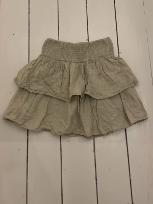 En grön gullig sommar kjol  - Söt grön kjol med dubbla volanger och bred smock i midjan. Kjolen har en luftig och avslappnad passform, perfekt för varma sommar dagar.