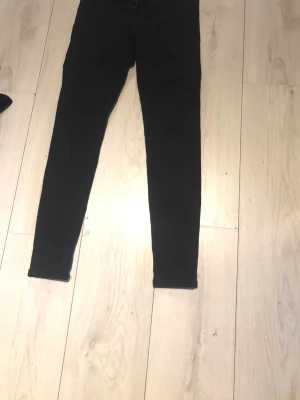 Svarta skinny jeans - Säljer ett par svarta skinny jeans med smal passform och klassisk femficksdesign. Jeansen har en enkel look utan synliga detaljer och passar perfekt till en avslappnad stil. Materialet är stretchigt jeans för extra komfort.