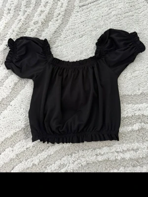 Svart offshoulder topp Gina Tricot - Trendig svart offshoulder topp från Gina Tricot med puffiga korta ärmar och resår vid hals, ärmslut och nederkant. Perfekt att styla med höga jeans eller kjol för en cool look.