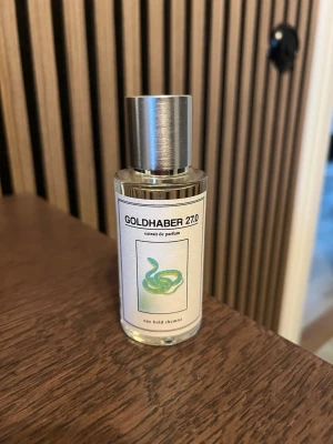 Goldhaber 27.0 parfym One Bold Chemist - Goldhaber 27.0 från One Bold Chemist är en exklusiv parfym i en genomskinlig glasflaska med silverfärgat lock. Etiketten har en grön orm och minimalistisk design. Innehåller bland annat denaturerad alkohol, parfym, limonen och citral. Tillverkad i Sverige.