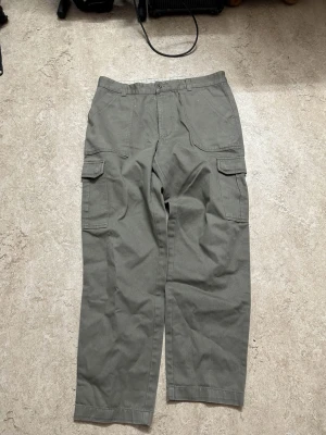 Gröna cargopants med raka ben - Snygga gröna cargopants med raka ben och klassiska cargofickor på sidorna. Byxorna har flera fickor både fram och bak, och är tillverkade i ett slitstarkt bomullstyg. Perfekta för en avslappnad streetstil.