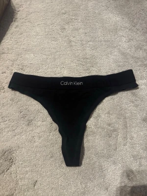 Calvin Klein svart string - Klassisk svart string från Calvin Klein i mjukt och bekvämt material. Minimalistisk design med logotyp. Skick: Mycket bra Storlek: S Märke: Calvin Klein Tidlös favorit som passar till allt. 