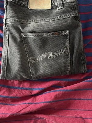 Svarta Nudie Jeans med raka ben - Säljer ett par svarta jeans från Nudie Jeans med klassisk kontrastsöm på bakfickorna. Jeansen har rak passform och är tillverkade i slitstark bomull. Perfekta för dig som gillar en clean och tidlös look. Modellen är slim Jim. W31 L34.
