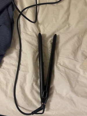 Svart plattång från Gratsis - Säljer en svart plattång från Gratsis med sladd och smal design. Plattången har en stilren look med detaljer i kopparfärg och är perfekt för att styla håret rakt eller vågigt. Enkel att använda och smidig att ta med sig.