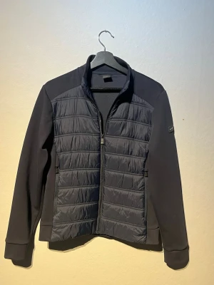 Ny Cardigan jacka Hacket london - NÄSTAN HELT NY Stilren mörk blå cardigan jacka från Hacket London i storlek XS. med quiltad front och släta ärmar. Jackan har dragkedja framtill, hög krage och diskret logga på ärmen. Perfekt för kyliga dagar och enkel att matcha med olika outfits.