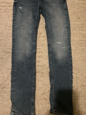 Slim Glenn jeans från Jack & Jones - Säljer ett par helt nya blå slim fit jeans från Jack & Jones, modell Glenn. Jeansen har slitna detaljer framtill, klassisk femficksdesign och normal midja. Materialet är mjukt jeans med lite stretch för extra komfort. Perfekta till vardagslooken.