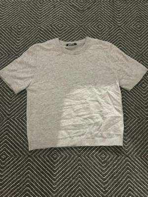 Grå basic t-shirt från Gina Tricot - En enkel och stilren grå t-shirt från Gina Tricot. T-shirten har rund halsringning och korta ärmar. Tillverkad i mjuk bomull som känns skön mot huden. Perfekt att matcha med jeans eller shorts för en clean look.