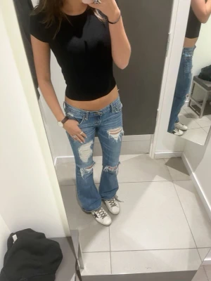 Wrangler bootcut jeans med slitningar - Säljer ett par blå bootcut jeans från Wrangler med låg midja och rejält slitna detaljer på både fram- och baksida. Midjemått är ca 40cm och innerben 77cm. OBS första bilden är inte min men jeansen har en liknelse till de 💕