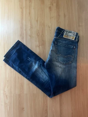 Replay Waitom jeans  - Säljer ett par Replay Waitom jeans i klassisk blå tvätt med slitningar. Jeansen har raka ben, snygga kontrastsömmar och hål på benen. Midja 41cm, längd 111cm. JAG SKICKAR EJ FLER BILDER NÄR JAG BÄR JEANSEN! för bättre inblick i passformen rekommenderar jag att googla på modellnamnet. För storleksguide kolla måtten noggrant då jeansen alltid kan vara uppsydda heller krympta och jag ej tar emot returer :) s6,1