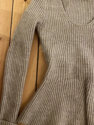 Beige ribbstickad tröja med v-ringning - Säljer en beige ribbstickad tröja med v-ringning och lång ärm. Tröjan har en figurnära passform upptill och blir lite utsvängd nedtill, vilket ger en snygg siluett. Perfekt för lager-på-lager under höst och vinter.