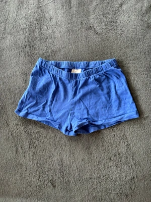 Blå shorts från H&M i bomull - Säljer ett par blå mjuka shorts från H&M i storlek 122/128. De har elastisk midja och är gjorda i tunn bomull, perfekta för varma dagar eller som chillplagg hemma. Klassisk enkel design utan mönster eller extra detaljer.