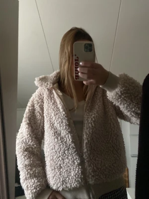 Beige teddyjacka från KappAhl - Mysig beige teddyjacka från KappAhl med dragkedja framtill och ribbade muddar. Jackan har en fluffig och mjuk struktur som ger en riktigt chill vibe. Perfekt för dig som vill ha en varm och stylish look under kyliga dagar. Som ny 