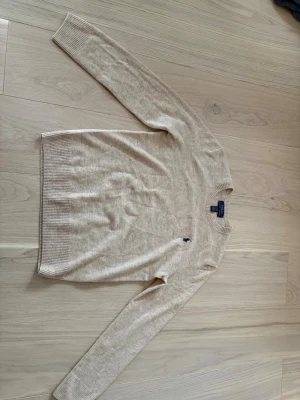 Beige stickad tröja Polo Ralph Lauren - Säljer en beige stickad tröja från Polo Ralph Lauren med klassisk rund hals och diskret logga broderad på bröstet. Tröjan har långa ärmar och ribbade muddar vid ärmslut och nederkant. Perfekt för lager på lager under hösten. Även helt oanvänd!