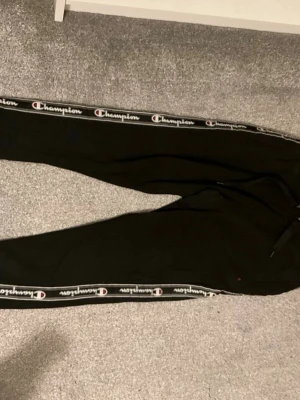 Svarta mjukisbyxor från Champion - Svarta mjukisbyxor från Champion med logga längs båda sidorna. Byxorna har snörning i midjan och är gjorda i mjukt material som passar perfekt för chill eller träning. Klassisk och sportig look med normal passform. Köpt för 500 kr säljs för 150