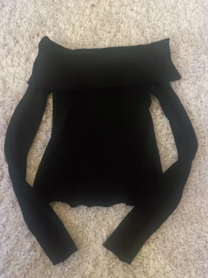 Svart offshoulder topp med långa ärmar - Säljer en svart offshoulder topp med långa ärmar. Toppen har en bred kant över axlarna som ger en snygg och stilren look. Materialet är stretchigt och följsamt, perfekt till många olika outfits. Använd ett fåtal gånger enbart hemma. Säljer då jag inte tycker den passar mig.  
