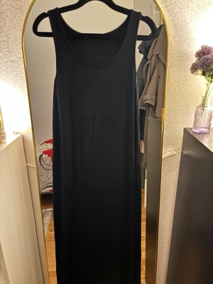 Svart långklänning i bomull - Enkel och stilren svart långklänning med ärmlös design och rund halsringning. Klänningen har rak passform och är tillverkad i mjuk bomull, perfekt för en clean och avslappnad look.