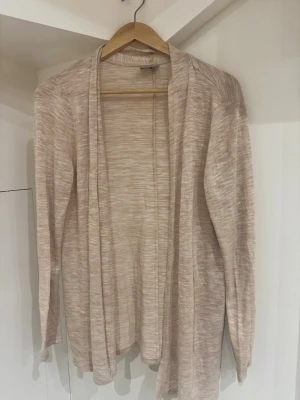 Beige kofta från Vero Moda, stl M - Lätt och tunn beige kofta från Vero Moda i storlek M. Koftan har ett diskret melerat mönster, lång ärm och öppen framtill utan knäppning. Perfekt att slänga över en topp för en chill och stilren look.