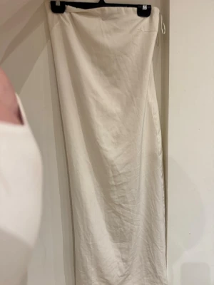 Vit långklänning från Gina Tricot - Säljer en stilren vit långklänning från Gina Tricot i storlek 34. Klänningen är axelbandslös och har en rak, enkel siluett med diskret dragkedja upptill. Perfekt för sommarens alla tillfällen!