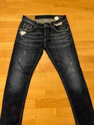 Mörkblå jeans från Dondup - Säljer ett par mörkblå jeans från Dondup med slitningar. Perfekta för dig som vill ha den där extra touchen på outfiten. Bara använda ett fåtal gånger. Hör av dig vid minsta fråga. Tja. 