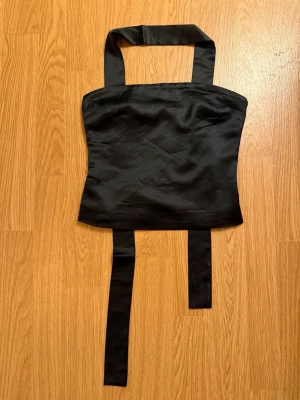 Svart scarf-topp i satin  - Supersnygg svart scarf-topp från Gina tricot i glansigt satinmaterial. Toppen har en scarf-detalj som runt halsen. Perfekt för att skapa en trendig och elegant look. Ny med prislapp och slutsåld på hemsidan!