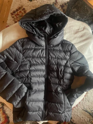 Svart pufferjacka från ONLY med huva - Säljer en svart pufferjacka från ONLY i storlek S. Jackan är i normal passform och går till midjan. Jackan har en stor huva, dragkedja framtill och quiltad design. Skicka 8/10. Skicka pm vid frågor. 