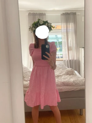 Rosa kortklänning med öppen rygg - Supersöt rosa kortklänning med puffärmar och volangkant. Klänningen har en snygg öppen rygg med twistad detalj och rund cut-out. Tillverkad i ett lätt och luftigt tyg. Enbart använt den en mindsommar. Är i storlek 158 