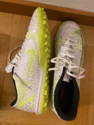 Nike Phantom GX fotbollsskor vit grusskor  - Säljer ett par Nike Phantom GX fotbollsskor i vitt med neon-gula detaljer och sula. Skorna har knappt användst och håller hög kvalité. Pris kan diskuteras 