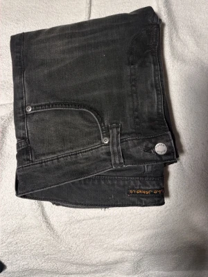 Mörk gråa jeans från Nudie Jeans Co - Säljer ett par svarta jeans från Nudie Jeans Co med klassisk femficksdesign och raka ben. Jeansen är använda 2-3 gånger och passar jätte bra nu till vintern!