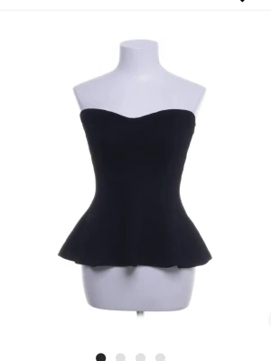 Svart ribbad bandeau tubtopp - Säljer en svart bandeau tubtopp med ribbad struktur och lätt utsvängd nederkant. Toppen är axelbandslös och har en figurnära passform som ger en snygg siluett. Perfekt att styla med jeans eller kjol för en trendig look.