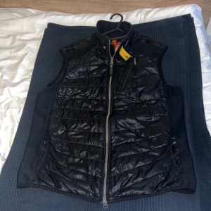 ParaJumper Väst - Säljer min Parajumper Zavier Warmup Väst.   Lätt, varm & stilren, perfekt till höst & vår. Använd - i bra skick. Jätte litet hål längst ner på baksidan, vilket man knappast ser. Det finns 6 olika fickor, 2 på insida, 1 bak och resten fram. Nypris ligger på 3000+kr. Passar bra för dig som är runt 170-180cm lång och 70-80kg. Tveka inte att ställa dina frågor, kom gärna med bud! Finns QR Scan + kod som verifierar att varan är äkta! Kvitto + annat finns tyvärr ej då jag fått denna som en gåva.