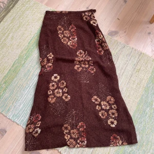 Brun blommig långkjol från Stefanel - Säljer en brun långkjol från Stefanel med blommigt mönster i beun. Kjolen har en rak siluett, dragkedja och knapp i sidan för stängning. Materialet känns mjukt och har ett fint fall, perfekt för dig som gillar vintagevibbar och unika prints. Storlek 38/34