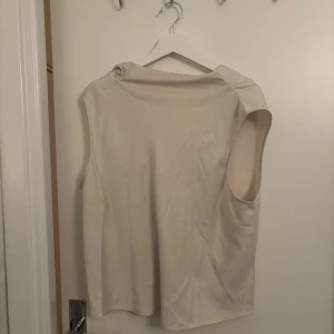 Beige ärmlös linnetopp - Säljer en stilren beige linnetopp med mjuk och slät yta. Toppen har en enkel design med breda axelpartier och ärmlös passform, perfekt för en clean och modern look. Passar dig som gillar minimalistiska plagg och ljusa färger.