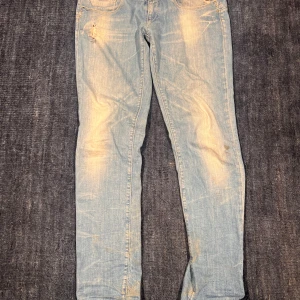 Replay ljusblå skinny jeans - Säljer ett par ljusblå skinny jeans från Replay med slitningar och snyggt tvättad look. Klassisk femficksmodell med Replay-logga på bakfickan och metallmärke vid fickan fram. Jeansen är i stretchigt denim och har smal passform.