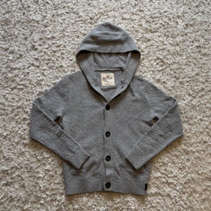 Grå stickad kofta/hoodie från Hollister - Snygg grå stickad kofta/hoodie från Hollister med knappar framtill. Den är använd men i mycket gott skick utan fläckar eller hål. Storlek S, tveka inte o skriva vid fler frågor!
