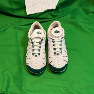 Nike Air Max sneakers vit/grön x Lacoste  - Nike Air Max sneakers i vitt och grönt med mesh och syntetmaterial. Snygga detaljer med gröna vågiga linjer, synlig Air Max-dämpning i sulan och snörning. Klassisk Nike Swoosh på sidan och broderad krokodil på plösen för extra stil.Liknande modell som originalet!