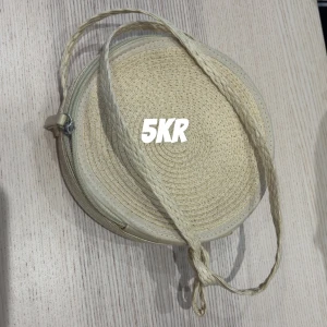 Rund axelväska i flätad stil - Säljer en rund axelväska i beige flätat material med dragkedja. Väskan har en lång axelrem och är perfekt för att bära det viktigaste. Enkel och stilren design som passar till många outfits.