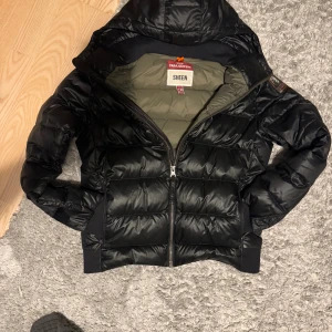 Svart Parajumper Sheen jacka - Säljer en glansig parajumper sheen jacka i barnmodell. Väldigt bra skick, flärpen på dragkedjan är lite sliten men det är enda defekten. Perfekt till vintern. Storlek M barn passar mellan 155-170cm skulle jag säga beroende på önskad passform. 