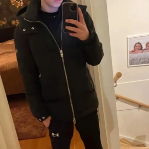 Svart J.lindeberg Jacka - Säljer en svart pufferjacka från J.lindeberg med stor huva och dragkedja framtill. Jackan har snygga detaljer som tryckknappar vid ärmslut och fickor med dragkedja. Perfekt för kalla dagar och riktigt skön att bära. Supersnygg jacka helt enkelt! Sen så kan pris diskuteras vid snabbt köp!