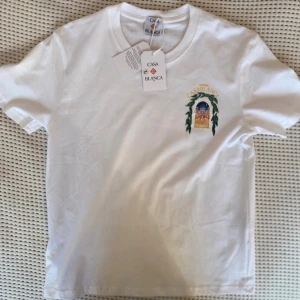  Casablanca T-shirt  - Vit t-shirt från Casablanca med färgstarkt tryck av en byggnad och gröna blad på bröstet och ryggen. Rund hals och korta ärmar. Trycket har detaljer i blått, rött, gult och grönt. Perfekt för dig som gillar unika motiv och stilrena plagg. 