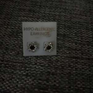 Silverfärgade örhängen med svart sten - Säljer ett par små, silverfärgade örhängen med svart sten i mitten och gnistrande detaljer runt om. Örhängena är hypoallergena och har klassisk stiftmodell. Perfekta för dig som gillar stilrena och glittriga accessoarer.