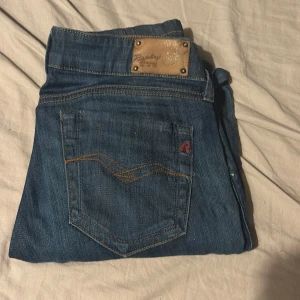 Replay jeans blå, midwaist, W28 L34 - Säljer ett par klassiska blå jeans från Replay med snygga detaljer på bakfickorna och läderpatch i midjan. Jeansen har normal passform och är tillverkade i slitstarkt denim. Perfekta för dig som gillar stilrena och tidlösa jeans. Jag tror att man inte kan köpa dom här någon stans dom har slutat att gjort den här modellen 