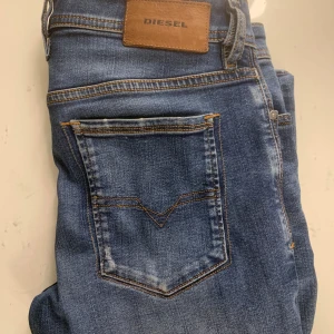 Blå slim-skinny jeans från Diesel - Snygga blå jeans från Diesel med klassisk femficksdesign och bruna kontrastsömmar. Jeansen har en smal passform och är tillverkade i stretchig denim för extra komfort. Märkespatch i läder baktill och diskret Diesel-logga vid fickan.