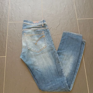 Blå jeans från Dondup - Snygga blå jeans från Dondup med skinny passform och klassisk femficksdesign. Jeansen har slitningar och ljusa tvättade partier som ger en cool, avslappnad vibe. Materialet är jeans med stretch för extra komfort. Perfekt för dig som gillar en smal siluett. Storlek 32 George model. Slitningar på högra knät.