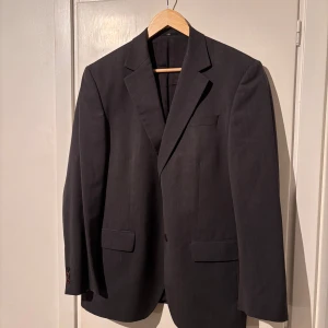 Mörkgrå klassisk kavaj - Snygg mörkgrå kavaj från sir of sweden med klassisk passform och två framfickor med lock. Kavajen har smala slag och knäppning framtill. Perfekt för en stilren look och passar till skjorta eller t-shirt.