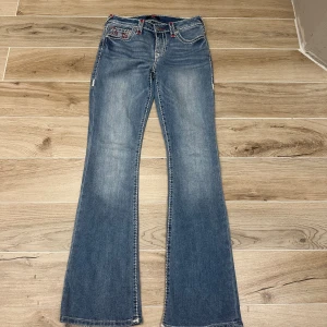 True Religion bootcut jeans blå storlek 27 - Blå jeans från True Religion med bootcut passform och kontrastsömmar i vitt och rött. Snygga detaljer på bakfickorna med röd och vit brodyr. Klassisk femficksmodell i mjukt denimtyg. Perfekta för dig som gillar en avslappnad men trendig look.