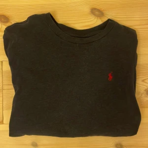 Marinblå långärmad tröja från Ralph Lauren - Marinblå långärmad tröja från Ralph Lauren med klassisk rund halsringning och rött broderat logotyp på bröstet. Tillverkad i mjuk bomull som känns skön mot huden. Perfekt för dig som gillar stilrena och enkla plagg med en touch av lyx.