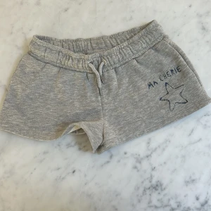 Grå mjukisshorts från Gina Tricot - Grå mjukisshorts från Gina Tricot med snörning i midjan och tryck med texten 'MA CHÉRIE' och en stjärna på ena benet. Perfekta för chill dagar eller träning. Sköna och enkla att matcha med din favorit-tshirt.